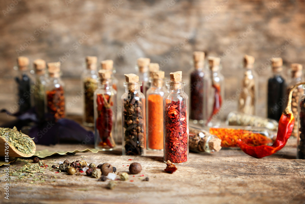 Assorted dry spices in glass bottles on wooden background