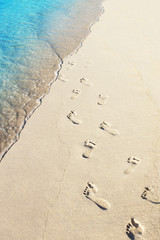 Wall Mural - Foot prints on a sandy beach with blue ocean wave on background