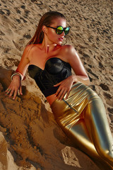 Wall Mural - Tanned girl on the sand in sun glass with wet hair and gold jewelry. Tanned girl lying on the sand. Gold tight pants. Black corset.