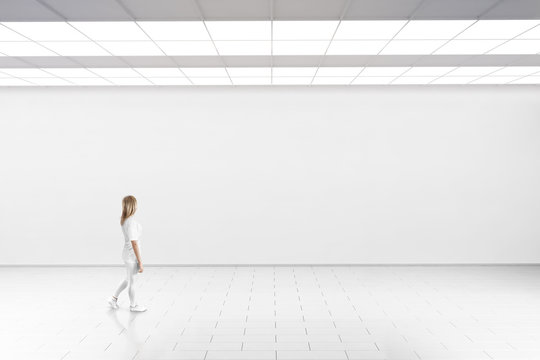 empty big hall wall mockup. woman walk in museum gallery with blank wall. white clear stand mock up 