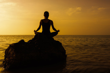 silhouette of woman practicing yoga on the rock during a beautif