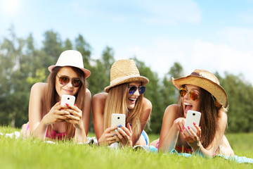 Happy group of friends lying on the grass and texting