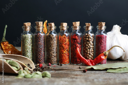 Different spices in small glass bottles on wooden table Canvas Print