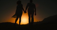 Couple Silhouette Running Away From Camera Holding Hands With The Sunset Golden Hour, The Sun A Warm Color, Slow Motion