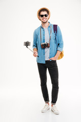 Wall Mural - Happy tourist holding backpack, camera and smartphone on selfie stick