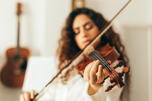 Girl Playing Violin. Young Woman Studying Music Alone At Home In The Living Room With Natural And Soft Light. Curly Long And Brunette Hair, Elegant Dressed.