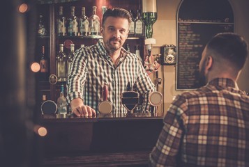 Wall Mural - Handsome bartender talking with customer at bar counter in a pub.