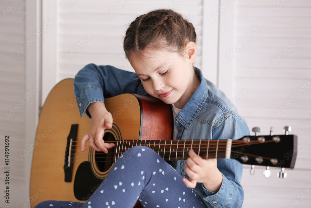 Little girl playing guitar on light background