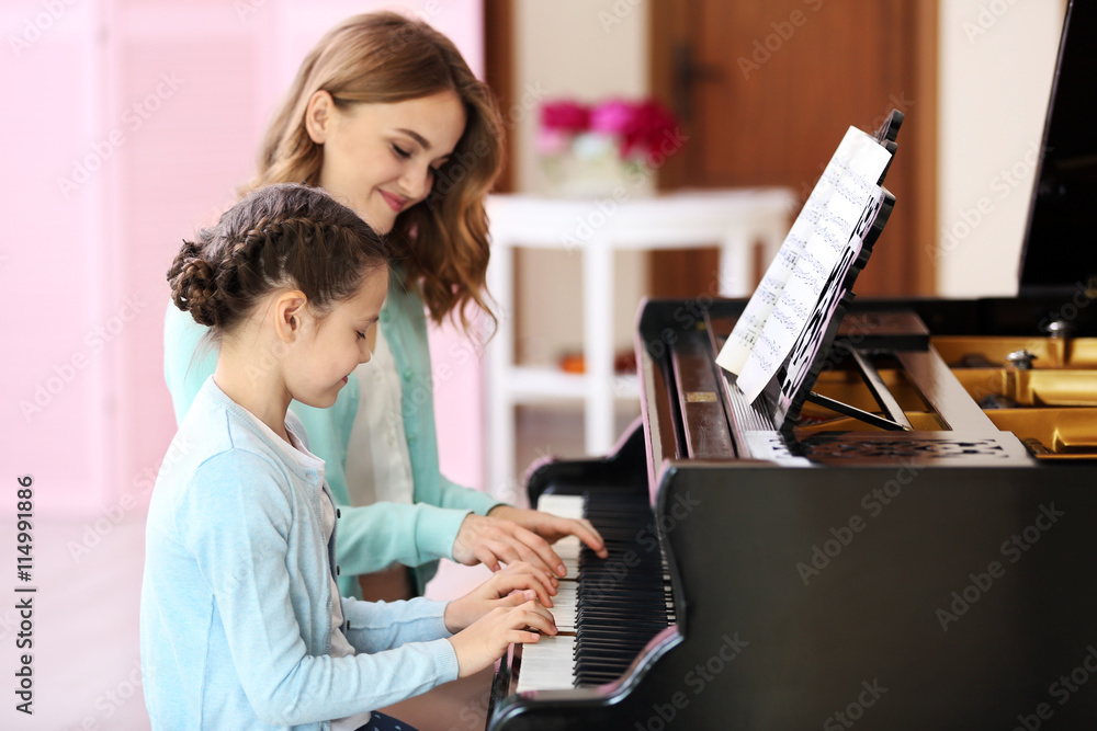Small girl learning play piano with teacher