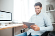 © Drobot Dean - Smiling businessman sitting and using tablet computer in office