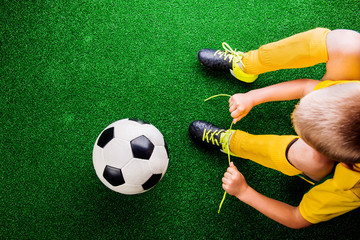 Unrecognizable little football player against green grass, studi