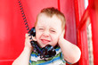 © EvgeniiAnd - kid hand closed his ears and squeezed his eyes shut while talking on the phone in a red telephone box. noisy surroundings, problem with phone connection