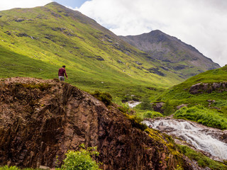 July 2nd 2016. Glencoe, Scotland, UK. Tourist admiring the view from the top of one of the waterfalls in Glencoe, Scottish Highlands, Scotland, UK