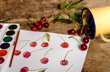 Paints, brush,  cherry, sketch, cup . Watercolor painting of ripe cherries on a wooden table.