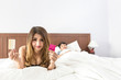 © Sasint - Beautiful young woman lying in bed confused about contraception. She is looking at contraceptive pills and condoms