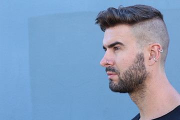 Wall Mural - Profile view of handsome stylish young man with undercut hairstyle, beard and piercings with copy space