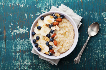 Wall Mural - Bowl of oatmeal porridge with banana, blueberries, almonds, coconut and caramel sauce on teal rustic table, hot and healthy food for Breakfast, top view, flat lay