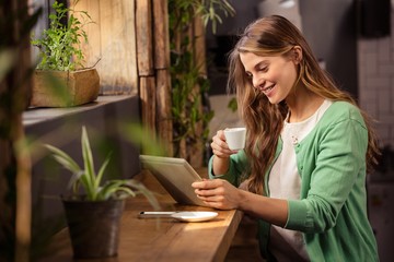 Wall Mural - Smiling woman drinking coffee and using tablet