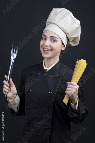 Fotografie, Obraz Cuoco donna su sfondo nero con posate e pasta in mano
