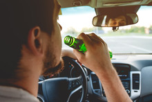 Drunk Young Man Driving A Car With A Bottle Of Beer. Don't Drink And Drive Concept. Driving Under The Influence. DUI, Driving While Intoxicated. DWI