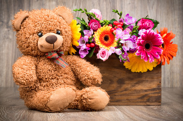 Beautiful flowers and a teddy bear on wooden background