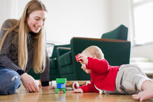 Woman And Baby Daughter Play With Building Blocks On Living Room Floor