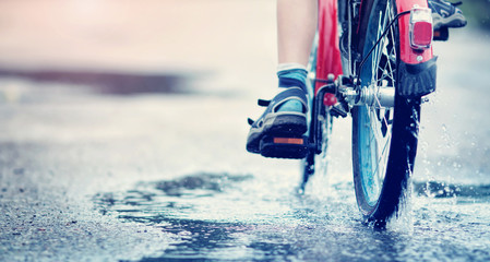 child on a bicycle at asphalt road in summer. Bike in the park moving through puddle on rainy day