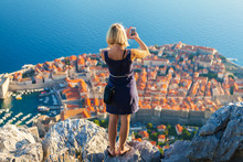 Female Traveller Make A Panoramic Photo Of The Old City Of Dubrovnik From The Mountain To Her Phone For Instagram Or Other Social Networks. Travel To Croatia. Summer Vacation.