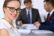 © rogerphoto - Portrait of a young business woman against a group of business people at a meeting.