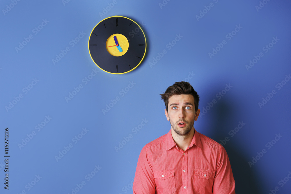 Man in a pink shirt standing beside a  big clock on blue wall