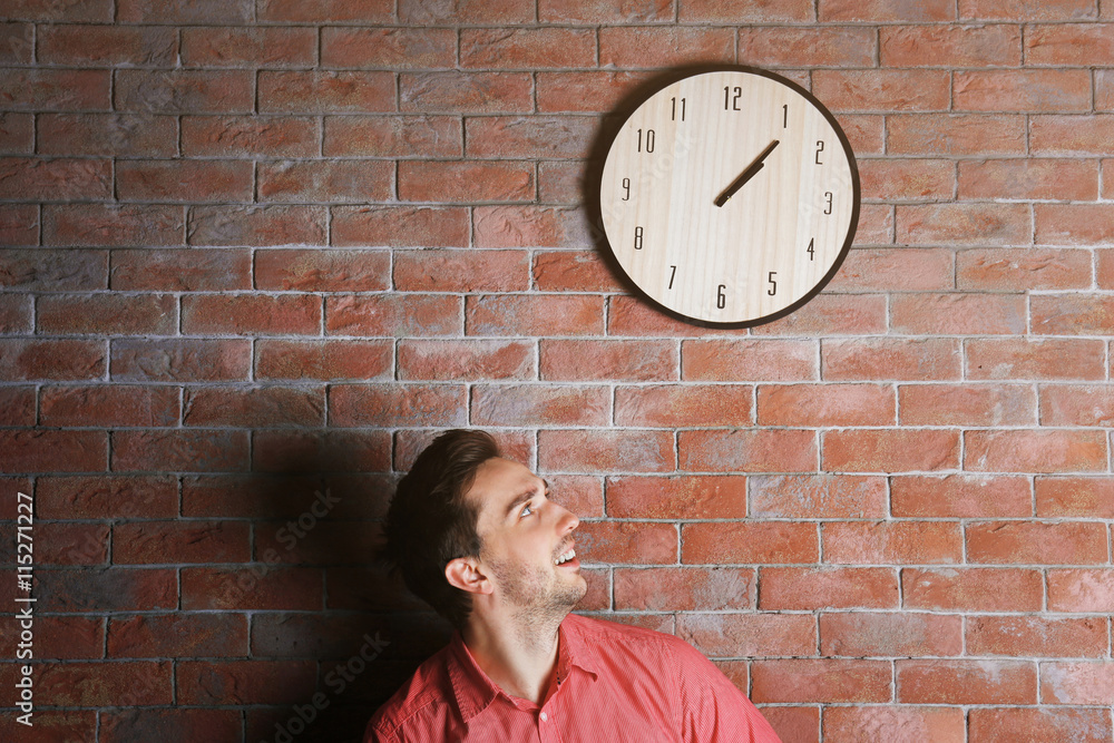 Man in a pink shirt standing beside a  big clock on a brick wall