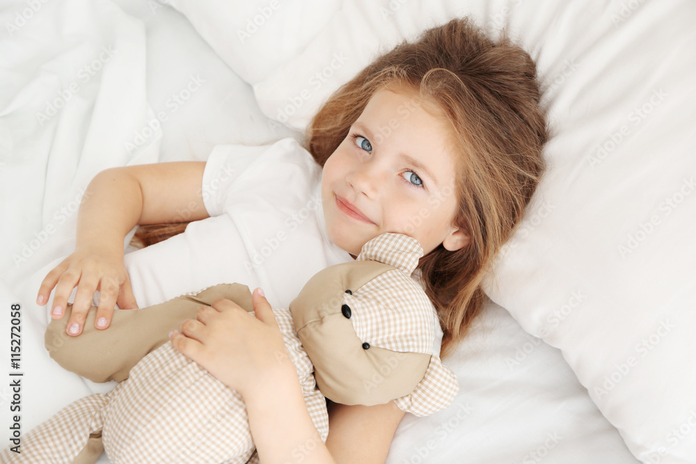 Adorable little girl hugging teddy bear in bed