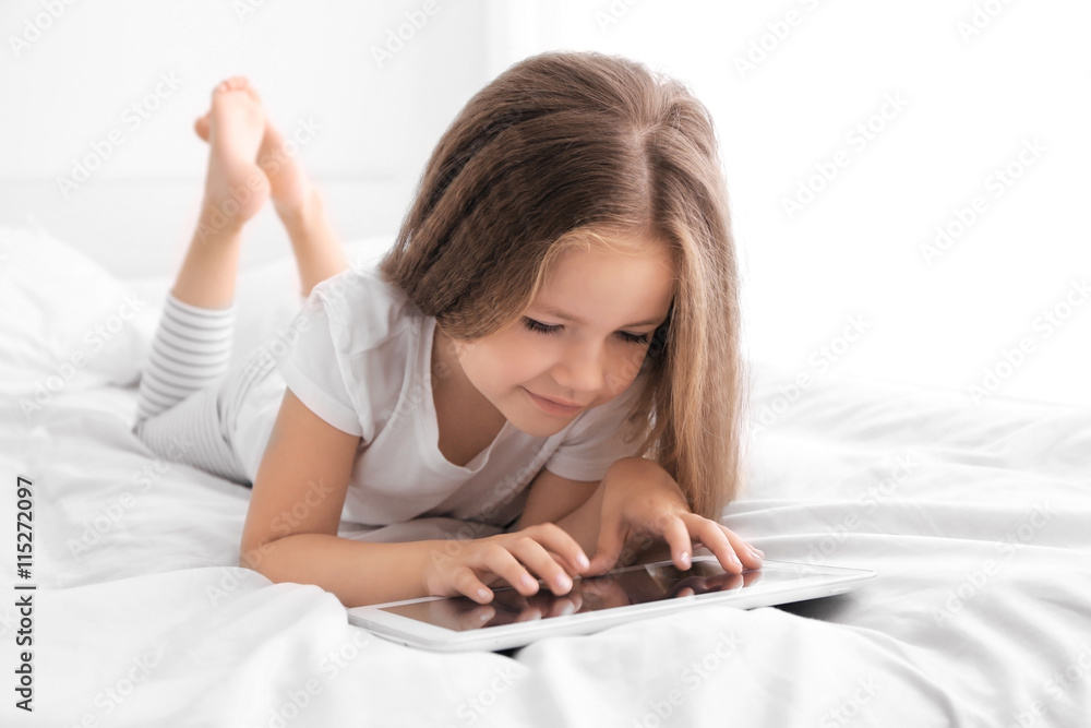Cute little girl playing with tablet on white bed