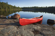 Red Canoe on Rocky Shore of Calm Lake with Pine Trees