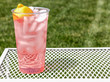 Fresh Squeezed pink lemonade it a clear cup outside on a lawn table.