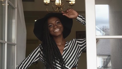 Wall Mural - Close-up of elegant sexy african american female model in black hat and striped dress smiling at the luxury apartments. Vogue fashion concept