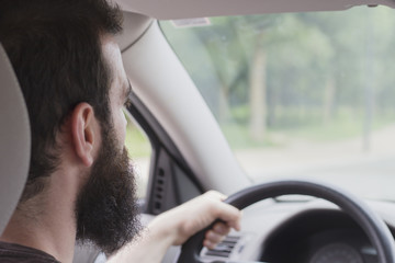 Young man with beard driving. Photo taken inside the car from behind.