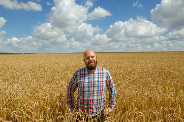 Happy smiling successful caucasian thirty years old farmer standing proud in front of his wheat fields.