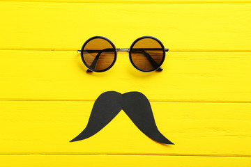 Sticker - Black sunglasses and mustache on a yellow wooden table