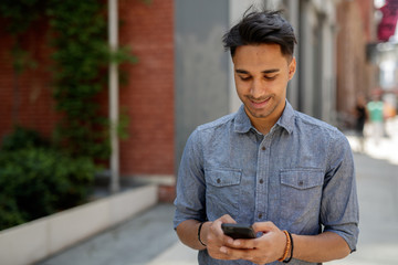 Wall Mural - Young Indian man in city texting cell phone