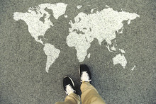 World Map On An Asphalt Road. Top View Of The Legs And Shoes. POV