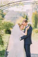 Charming groom and bride softly embracing at wedding day. Sunny summer park on background