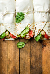 Wall Mural - Healthy lunch snack. A row of tortilla wraps with grilled chicken fillet and fresh vegetables on rustic wooden background