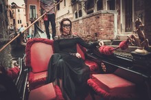 Beautiful Woman In Black Dress With Carnaval Mask Riding On Gondola. 