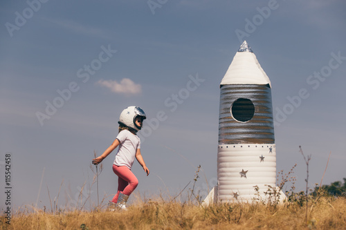 Zdjęcie XXL Szczęśliwa dziecko dziewczyna ubierał w astronauta kostiumu bawić się z ręcznie robiony rakietą. Lato na zewnątrz