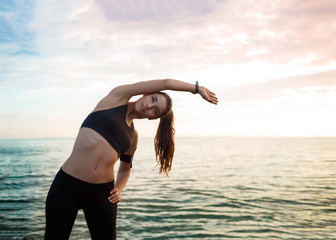 Wall Mural - Picture of young beautiful fitness girl makes sport exercises with sea on background