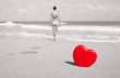 Heartbreak and active lifestyle concept. Heart on the beach with woman walking away in the distance.
