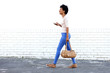 © mimagephotos - Beautiful woman walking and listening to music with purse