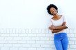 © mimagephotos - Smiling woman standing with arms crossed by white wall