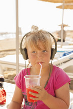 Turkey, Alanya, Portrait Of Blonde Girl (4-5) Wearing Headphones And Drinking With Straw On Beach